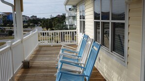 Een houten terras met witte relingen en blauwe schommelstoelen.