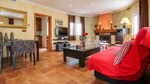 A living room with a red sofa, a TV, a fireplace, and a dining area with chairs and a table. - Beautiful home in Orihuela (Orihuela)