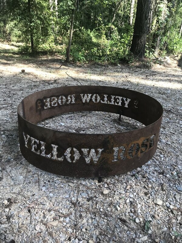Un anillo de fuego metálico con la inscripción “YELLOW WOLF 1953” en un área boscosa.