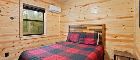 A wooden cabin bedroom with a bed, a window, and a ceiling fan.