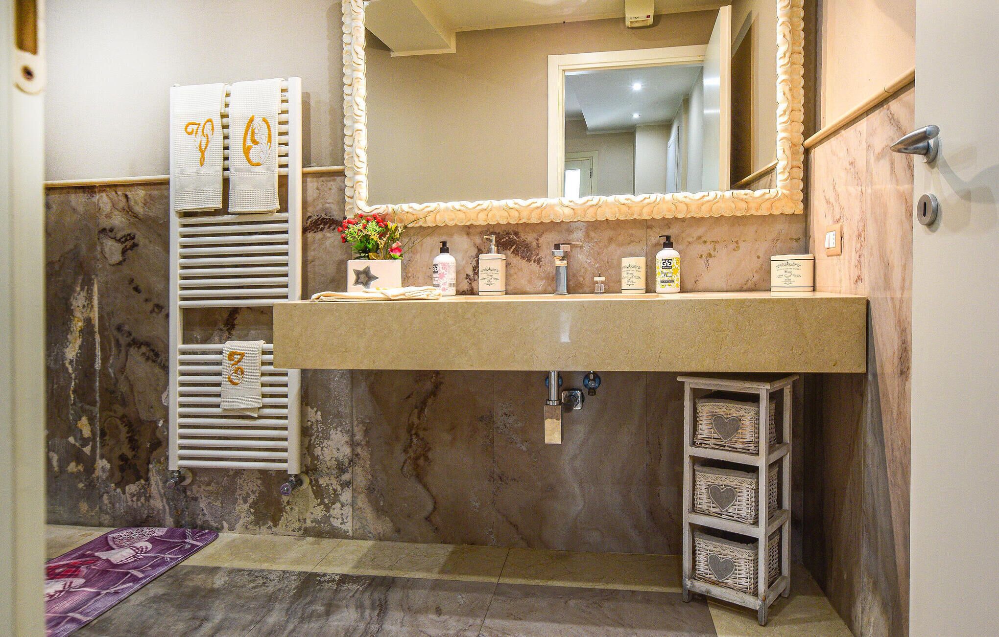A bathroom with a marble sink, a mirror, and a shelf with toiletries.