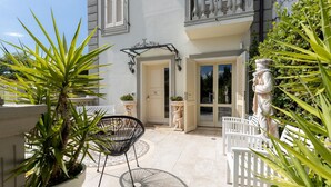 Une terrasse avec une chaise blanche, un pot de fleurs et une statue.