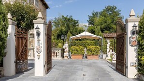 Une entrée fermée par un portail, agrémentée d’un auvent, de statues et d’un jardin bien entretenu.