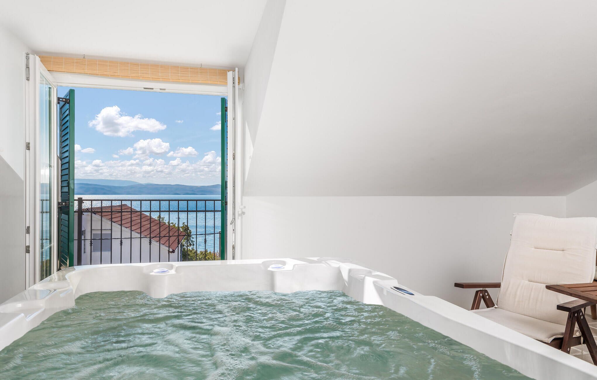 A room with a hot tub, a balcony with a view of the sea, and a chair.