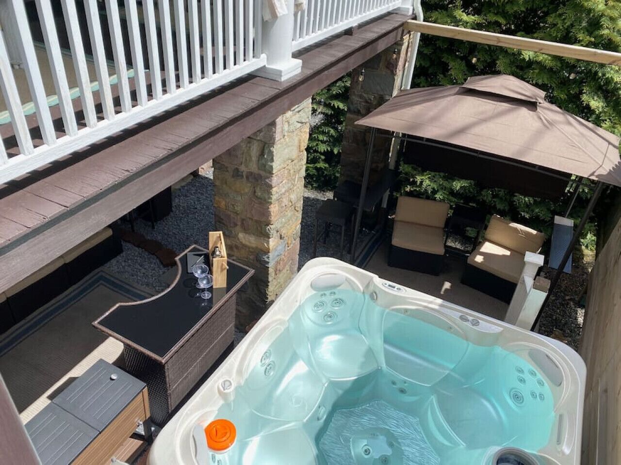 A hot tub with a wooden deck and stone pillars, surrounded by outdoor furniture and a covered seating area.