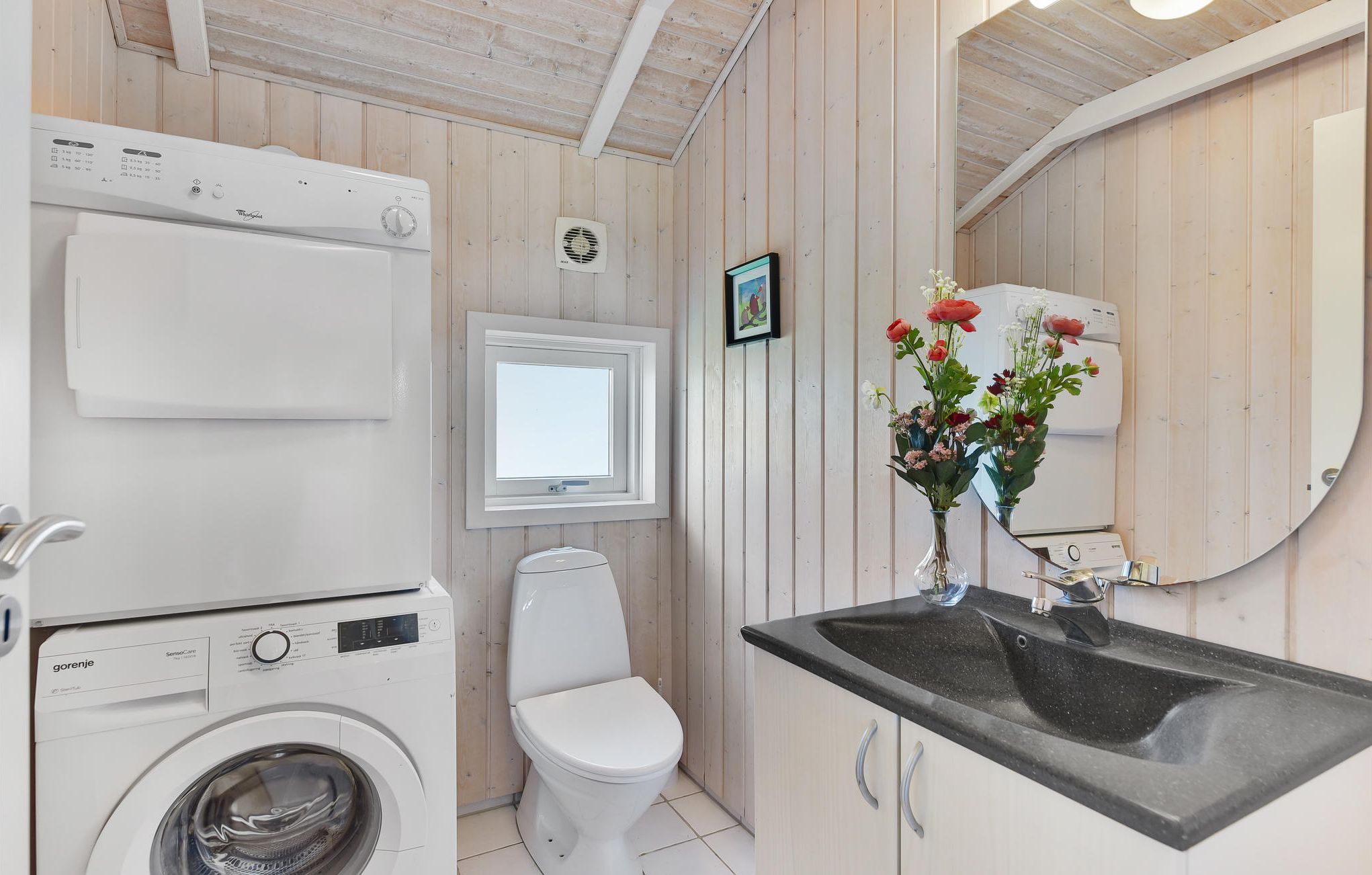 Une petite salle de bain équipée d’un lave-linge, de toilettes, d’un lavabo et d’un miroir.