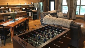 A cozy living room with a foosball table, a sofa, and a dining area with a wooden table and chairs. - BUCKEYE Creekside Cabin Ride to the trails from the cabin (Combs)