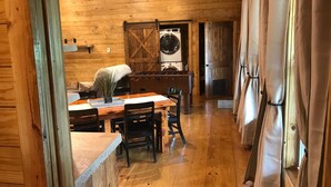 A wooden interior with a dining table, chairs, a foosball table, a washing machine, and a large door. - BUCKEYE Creekside Cabin Ride to the trails from the cabin (Combs)