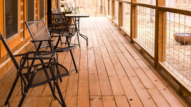 A covered wooden deck with metal chairs and tables, overlooking a forested area. - BUCKEYE Creekside Cabin Ride to the trails from the cabin (Combs)