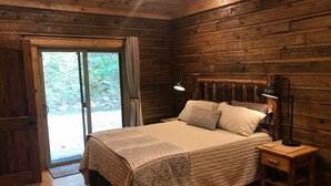 A wooden cabin bedroom with a bed, bedside lamps, and a view through a glass door. - BUCKEYE Creekside Cabin Ride to the trails from the cabin (Combs)