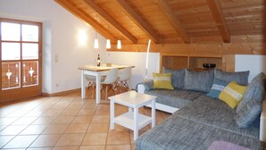 Una sala de estar acogedora con techo de madera, un sofá, una mesita y un comedor con sillas.