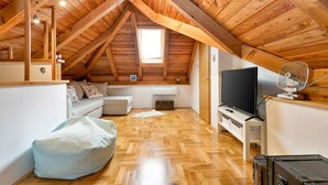 A cozy attic room with wooden beams, a white sofa, a bean bag, a TV, and a fan. - Pet friendly home in Piscanovec (Piscanovec)