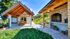 A covered outdoor area with a wooden table and benches, a brick oven, and a garden with a hedge and flowers. - Pet friendly home in Piscanovec (Piscanovec)
