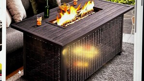 Un área de estar al aire libre rectangular con una chimenea integrada, una mesa de vidrio y un sofá acolchado con cojines.