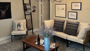 A living room with a wooden coffee table, a blue vase with lavender, a sofa with patterned cushions, a chandelier, and framed artwork on the walls. - Casita in the Oaks (Canyon Lake)
