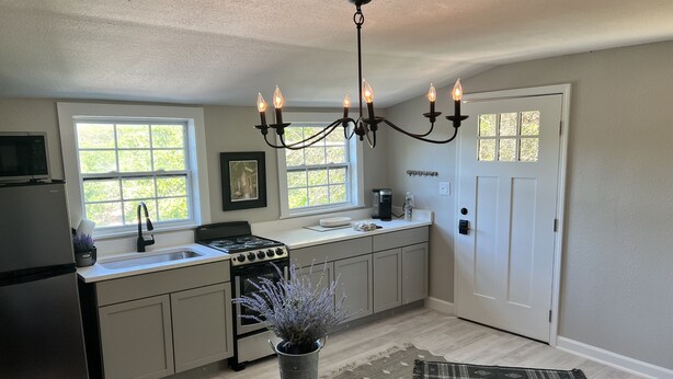 A kitchen with a stove, sink, and a chandelier. There is a door and a window with a view of greenery. - Casita in the Oaks (Canyon Lake)