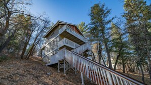 A wooden cabin with a balcony and stairs, surrounded by trees. - Lunar Lodge -  Forest Views | Fireplace | Smart TV (Big Bear Lake)