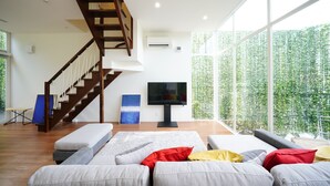Uma sala de estar ampla com escada de madeira, TV de tela plana e uma grande janela com vista para o verde.