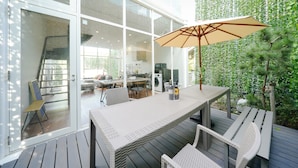 Uma área moderna para refeições ao ar livre, com mesa, cadeiras, um grande guarda-sol e um deck de madeira.