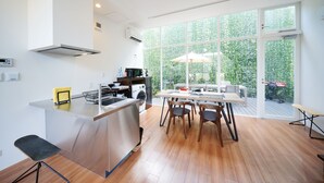Cozinha moderna com ilha central, mesa de jantar de madeira e cadeiras. Há uma janela grande com vista para o verde lá fora.