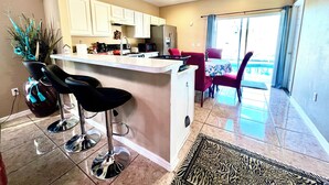 A modern kitchen with white cabinets, a central island, and a dining area with red chairs.
