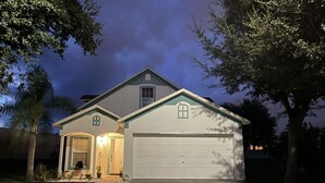 A two-story house with a garage, a front porch with a chair, and a well-maintained lawn.