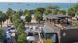 A beachfront hotel with outdoor seating, palm trees, and boats in the background. - The Chezz Condominium by Patsamon (Pattaya)
