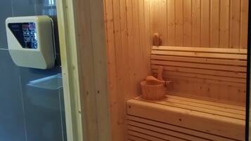 A sauna with wooden walls and benches, a control panel, and a small wooden table.