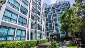 A modern multi-story hotel with a clean, white facade, large windows, and a well-maintained garden area with steps leading to the entrance. - The Chezz Condominium by Patsamon (Pattaya)