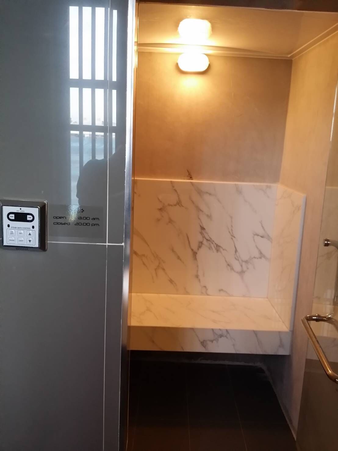 A bathroom with a marble wall, a light fixture, and a control panel.