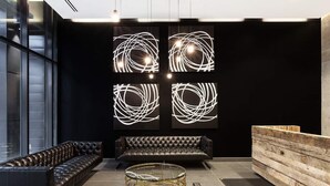 A modern lobby with a leather sofa, a round glass coffee table, and abstract wall art. - Cozy Skyline Entire Condo in Downtown - Across from Bell MTS Centre (Winnipeg)