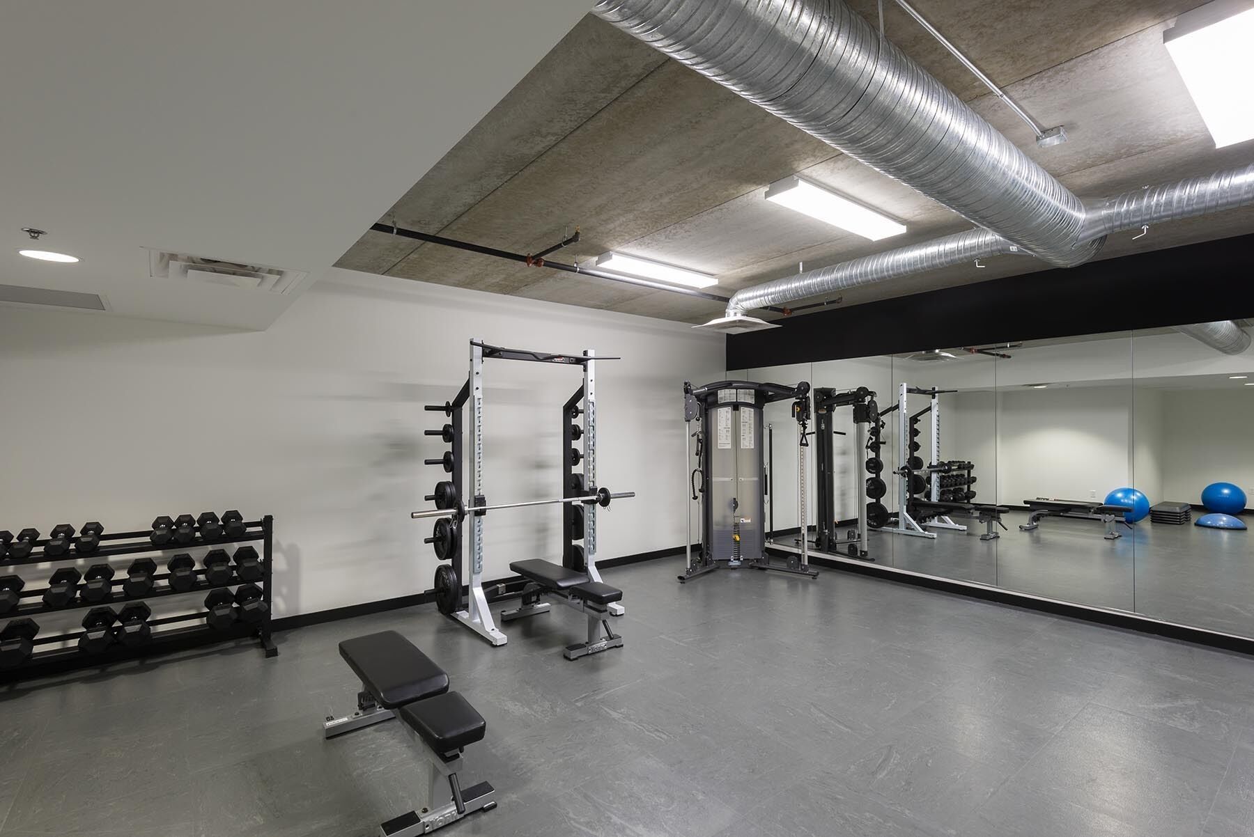 Une salle de sport équipée de matériel de musculation, de bancs et dotée d’un mur recouvert de miroirs.