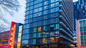 A modern high-rise building with a glass facade, a prominent 'PARK' sign, and a parking garage entrance. - Cozy Skyline Entire Condo in Downtown - Across from Bell MTS Centre (Winnipeg)