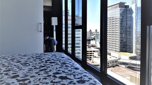 A hotel room with a large window offering a city view, a bed with a floral-patterned bedspread, and a visible closet. - Cozy Skyline Entire Condo in Downtown - Across from Bell MTS Centre (Winnipeg)
