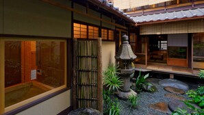 Un bâtiment japonais traditionnel doté de portes coulissantes, d’une lanterne en pierre et d’un jardin agrémenté de rochers et de plantes.