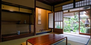 A traditional Japanese room with tatami flooring, a low wooden table, sliding shoji doors, and a view of a garden.
