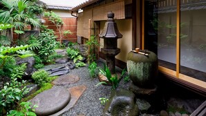Un jardin japonais traditionnel agrémenté d’une lanterne en pierre, d’une clôture en bambou et de diverses plantes.
