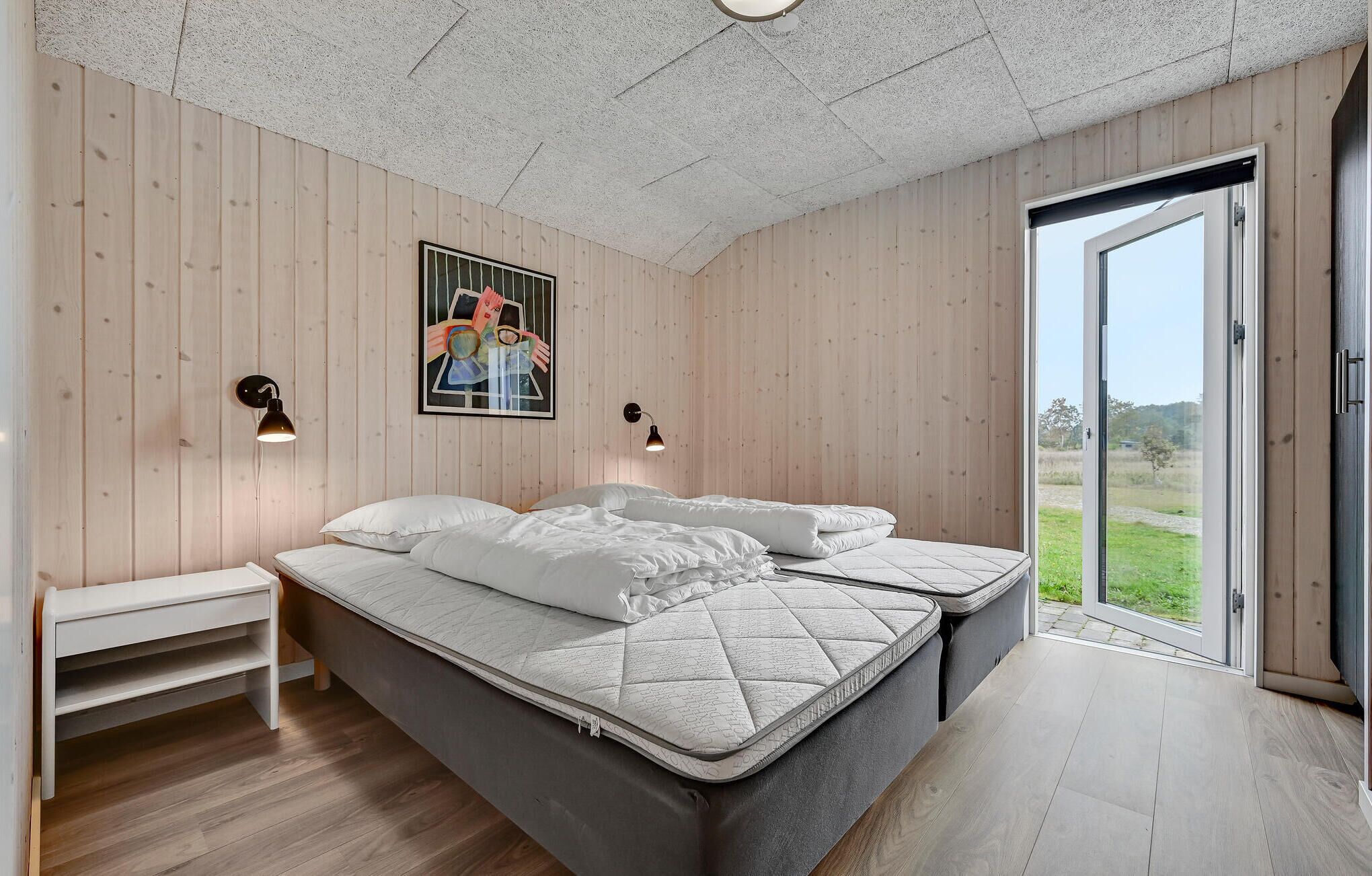 A bedroom with a large bed, two bedside tables, a wall-mounted picture, and a door leading to an outdoor area.