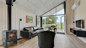 Una sala de estar moderna con una estufa de leña, un sofá de cuero, un televisor y un ventanal con vistas al exterior.