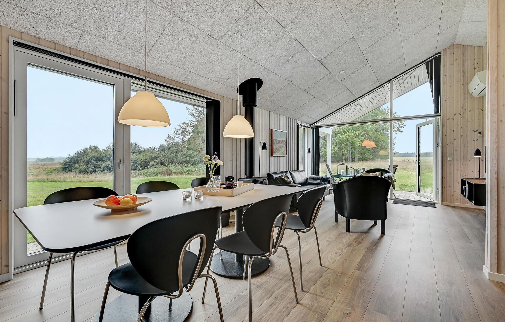 A modern dining area with a long table, black chairs, and pendant lights.