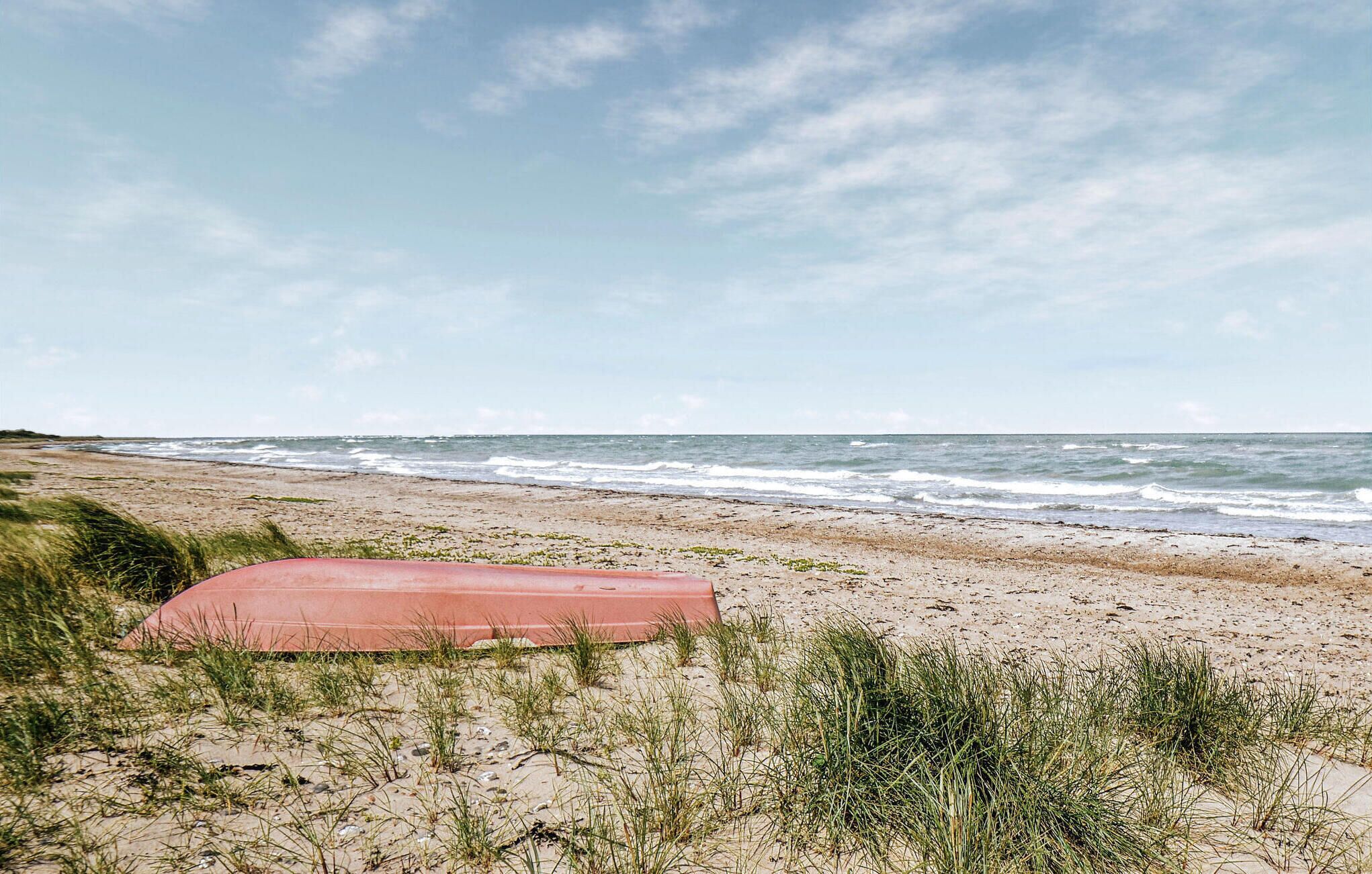 Ein Strand mit einem roten Boot im Sand, Wellen im Hintergrund und grasbewachsenen Dünen.