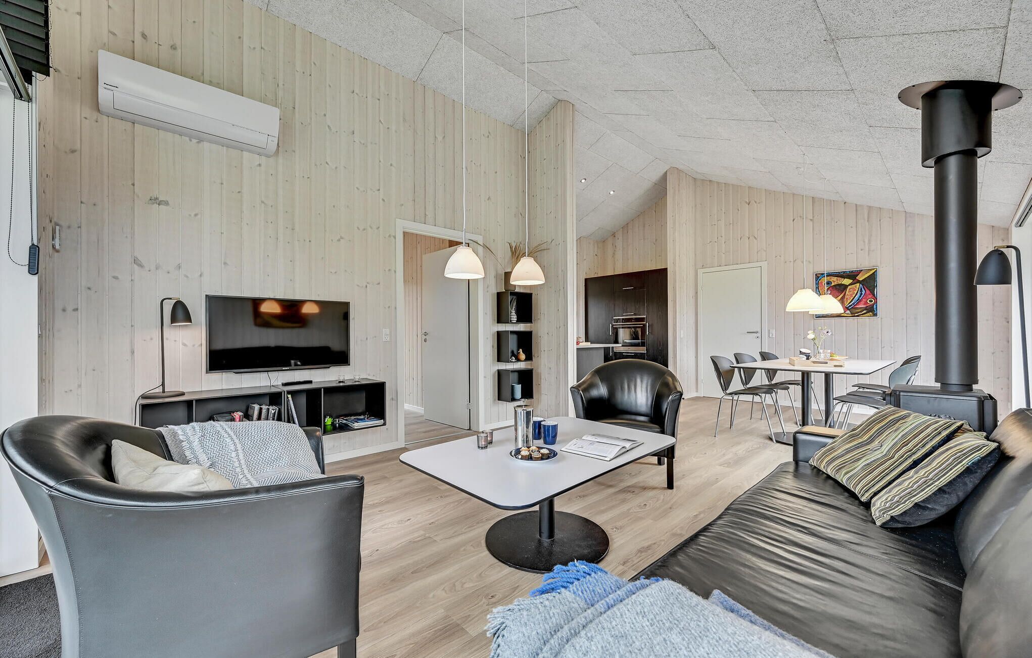 Ett modernt vardagsrum med en platt-TV, en soffa i läder, ett matbord och en vedkamin.