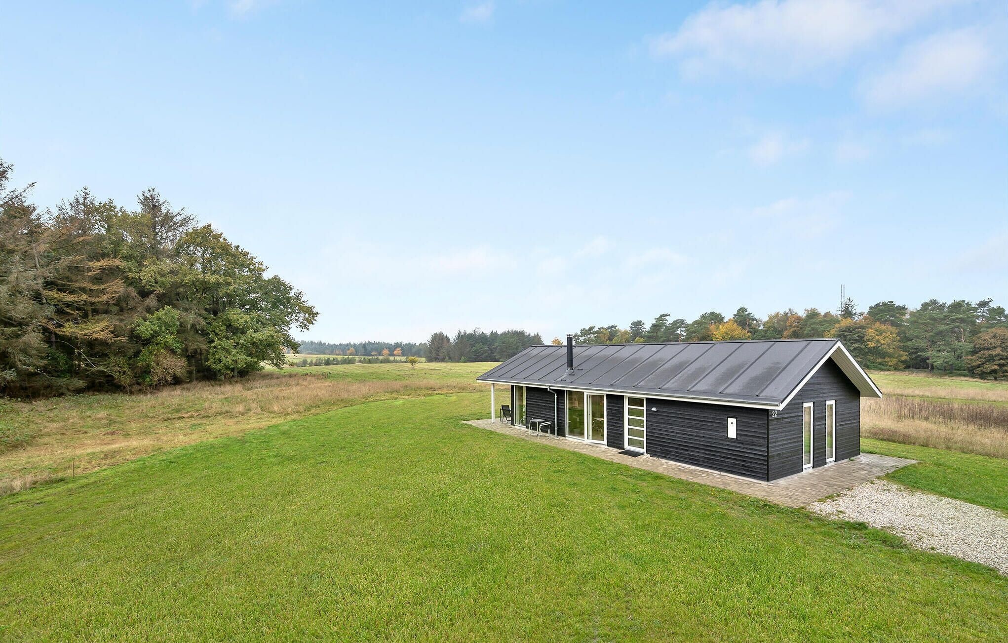 Een laag gebouw met een donkere buitenkant en een schuin dak, gelegen in een grasveld met bomen op de achtergrond.