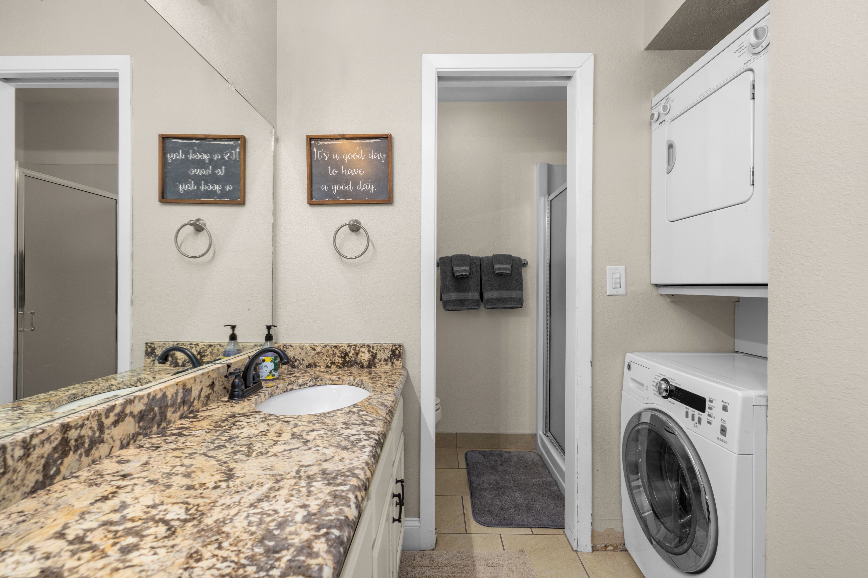 A bathroom with a granite countertop sink, two towel racks, a white washing machine, and two motivational wall signs.