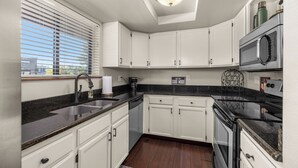 A modern kitchen with white cabinets, a black countertop, a built-in microwave, and a coffee maker. - 2 bedroom condo in Downtown Whitefish, Close To Glacier Park, Skiing And Golf (Whitefish)