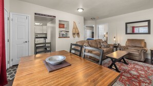 A spacious living area with a wooden dining table, a sofa, and a leather armchair. There is a kitchen in the background, a bookshelf, and a mirror on the wall. - 2 bedroom condo in Downtown Whitefish, Close To Glacier Park, Skiing And Golf (Whitefish)