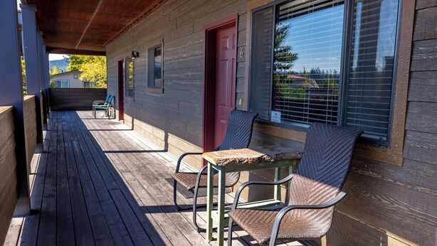 A wooden deck with two chairs and a table, a red door, and a window with blinds. - 2 bedroom condo in Downtown Whitefish, Close To Glacier Park, Skiing And Golf (Whitefish)