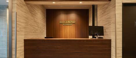 A reception desk with a wooden finish and a sign that reads "HOTEL TREND KYOBASHI".