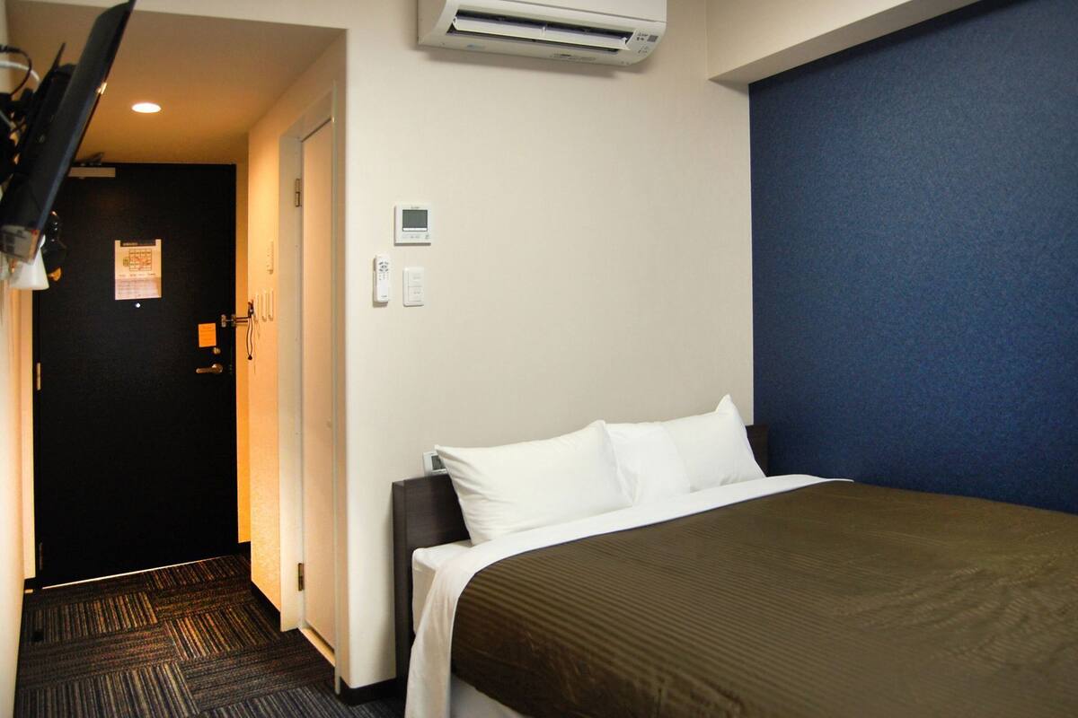 Una habitación de hotel con cama, aire acondicionado de pared, una puerta con cartel y suelo alfombrado.