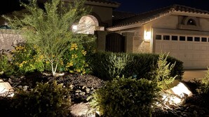 A residential house with a garage, a well-maintained garden with various plants and a stone pathway, and a moon visible in the sky. - Luxury Lakeside Home! Private Pool, Dock, Outdoor Kitchen, & Private Courtyard! (Glendale)